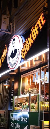 Dükkânın gece cephesi: yanan ADAM GİBİ ve ÇİĞKÖFTE tabelaları, ortada Özcan Usta logosu ve vitrin.