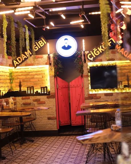 Salon: tuğla duvarlar, ortada ışıklı logo panosu, kırmızı salon kapıları ve ahşap masalar.